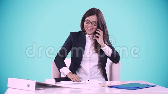 商务女性坐在办公桌前微笑在蓝色背景后面她在打电话关于视频的预览图