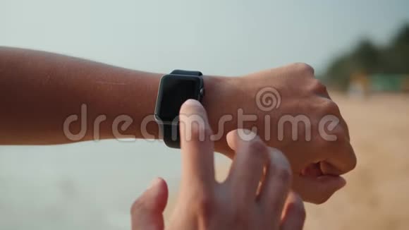 活跃的生活方式男人看科技智能手表特写宏观特写手臂沙滩触摸屏上的腕带视频的预览图