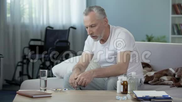 坐在沙发上吃药的老年残疾男性孤独和悲伤视频的预览图