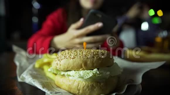 一个女孩和一个男人在你的智能手机上拍照你的汉堡在酒吧视频的预览图