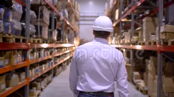 跟踪员工男性仓库工人工程师戴安全帽工作的镜头穿过物流中心视频的预览图