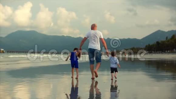 年轻的家庭一个父亲和他的儿子和女儿沿着海岸在海岸上散步幸福的家庭散步视频的预览图