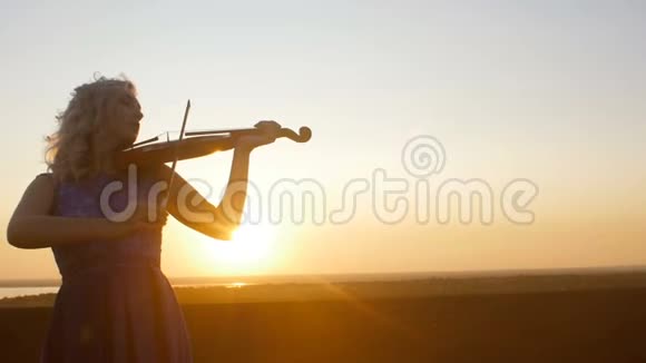 一位年轻女子在阳光下的剪影吹着小提琴女孩沿着音乐的琴弦放松和移动视频的预览图