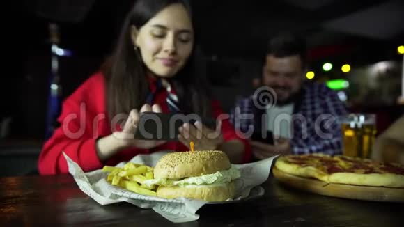 一个女孩和一个男人在你的智能手机上拍照你的汉堡在酒吧视频的预览图