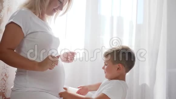 小儿子在室内听肚子大的准妈妈肚子视频的预览图