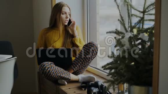 性格开朗的女摄影师在家拿着相机和笔记本电脑坐在窗台上打电话视频的预览图