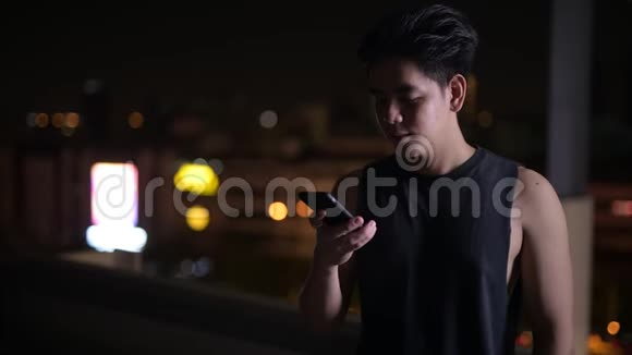 年轻快乐的亚洲男人夜间在户外使用电话的肖像视频的预览图