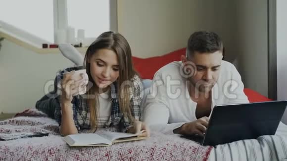 幸福夫妻在家休息早上躺在床上看书用笔记本电脑的年轻男女视频的预览图