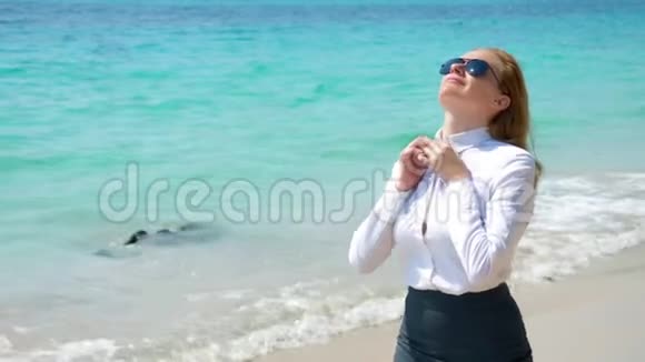 在海滩上戴太阳镜的女商人她在大海和太阳中快乐她解开衬衫扣子呼吸着视频的预览图