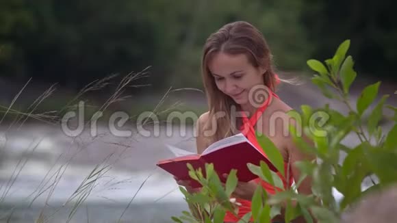 女孩在河流和前景的分支阅读书籍视频的预览图