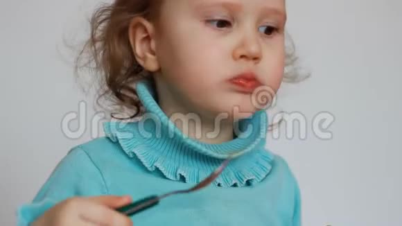 一个漂亮的小女孩坐在桌子旁用盘子里的勺子吃食物这孩子仔细咀嚼早餐视频的预览图