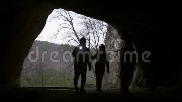 年轻的徒步旅行者戴着头盔从森林进入黑暗的洞穴手电筒视频的预览图