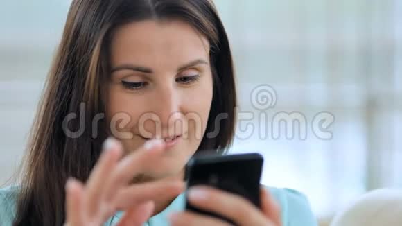 年轻快乐的女人在室内沙发上用智能手机视频的预览图