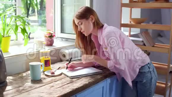 年轻女孩站在厨房做笔记的场景视频的预览图