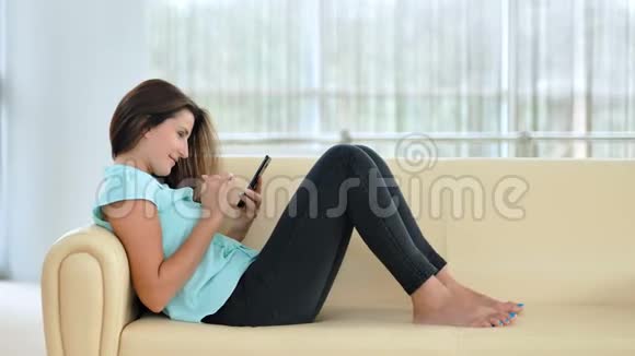 年轻快乐的女人在室内沙发上用智能手机视频的预览图