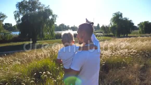 年轻的爸爸在草地上抱着他的孩子父子俩指着太阳看着田野家庭幸福支出视频的预览图