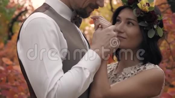 一个穿着白色衬衫的男人吻一个穿着白色裙子女孩的手她站在秋天的公园里视频的预览图