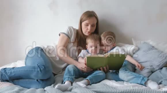 家庭妈妈和两个双胞胎兄弟蹒跚学步的孩子在床上看书家庭阅读时间视频的预览图