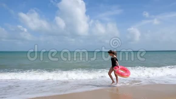 快乐的年轻女子带着甜甜圈漫步在热带海滩度假穿泳装的放松女人在海滩上玩得开心视频的预览图