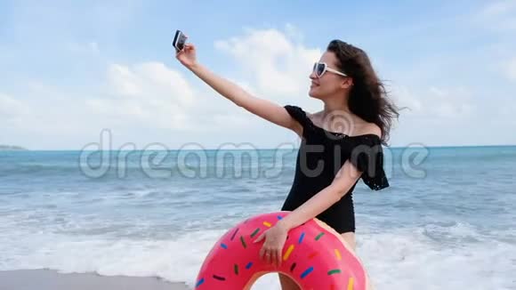 年轻的女人带着甜甜圈和太阳镜在热带海滩度假时玩得开心享受暑假放松放松视频的预览图
