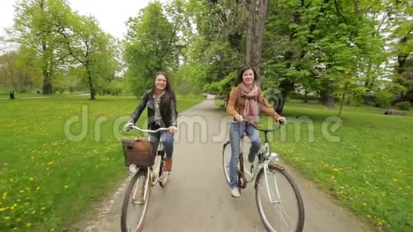 两个女朋友在春天骑自行车在公园里前视图相机在运动视频的预览图
