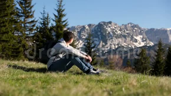 背着背包的年轻旅行家站在山顶上欣赏着迷人的景色游客用智能手机拍照视频的预览图