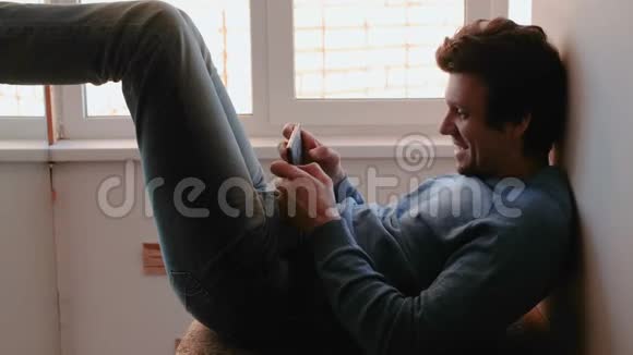 有电话的人快乐的年轻人坐在靠近窗户的阳台上玩手机游戏视频的预览图