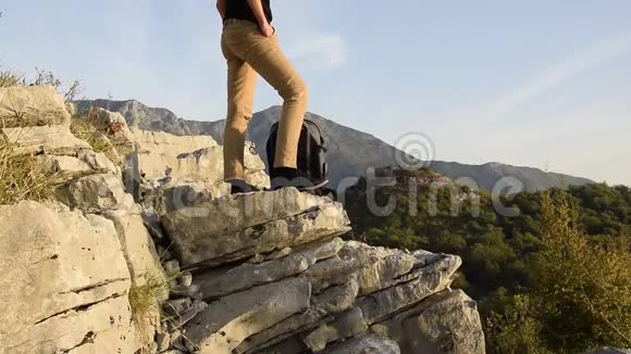 女徒步旅行者的双腿站在山崖的边缘与美丽的山峰对峙视频的预览图