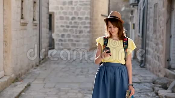 戴着帽子兴高采烈的女游客用现代化的手机设备在街上走来走去积极的旅行者视频的预览图