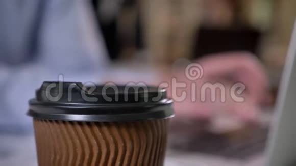 办公室里桌子上的棕色咖啡杯商人的手在背景上的笔记本电脑上打字背景模糊视频的预览图