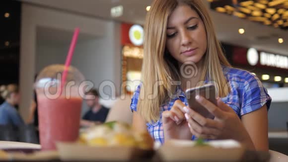 年轻可爱的女士穿着蓝色格子衬衫在咖啡厅使用智能手机视频的预览图