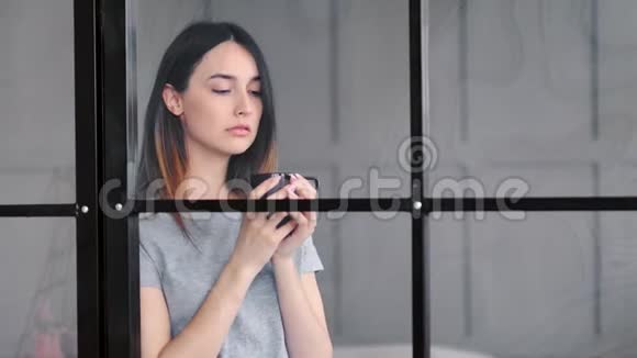 年轻漂亮的女人在家的窗户后面喝咖啡视频的预览图