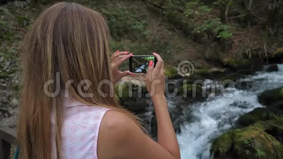 一位年轻女子站在山溪旁用智能手机拍摄视频视频的预览图