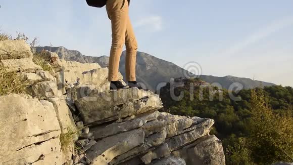 女徒步旅行者的双腿站在山崖的边缘与美丽的山峰对峙视频的预览图