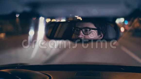 年轻的商人开着他的车在一个夜晚的城市后视镜反射视频的预览图