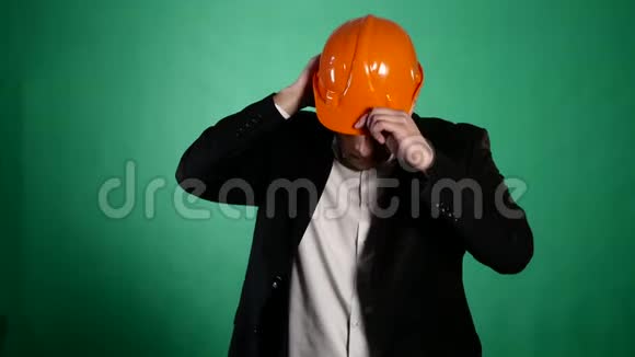 一个穿着橙色建筑头盔和西装的迷人男人看着相机一个年轻的工人用他的视频的预览图