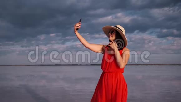 年轻的女人在一个美丽的不寻常的地方自拍穿着红色裙子帽子和太阳镜的女孩在粉红色的湖上视频的预览图