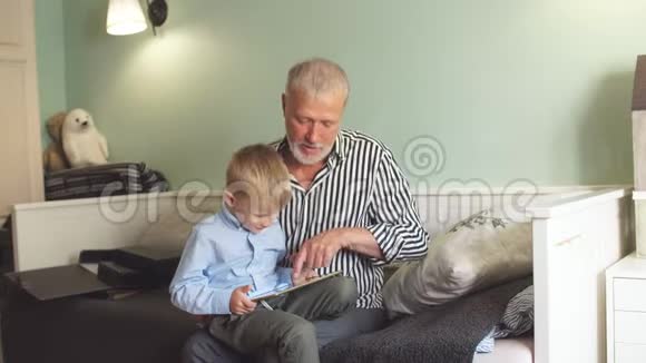 祖父和孙子坐在沙发上用数码平板电脑视频的预览图