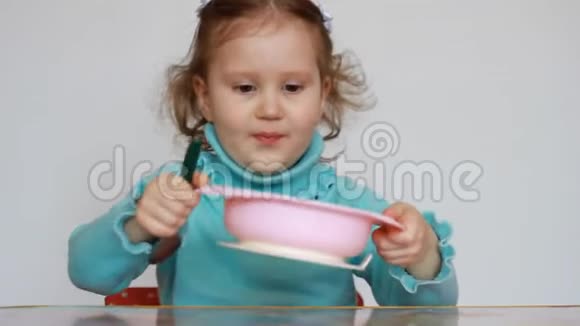 一个漂亮的小女孩坐在桌子旁用盘子里的勺子吃食物这孩子仔细咀嚼早餐视频的预览图