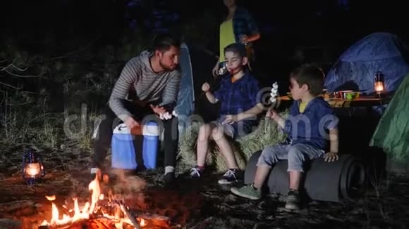 家庭旅行爸爸为旅途中的孩子讲故事妻子为丈夫带来饮料在篝火旁与儿子交谈视频的预览图