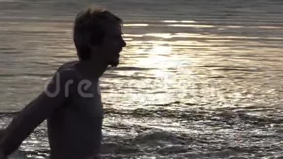 滑稽的男人在夕阳西下的时候在湖中掀起水流视频的预览图