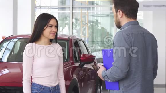 漂亮的幸福女人在收到汽车钥匙后与汽车经销商握手视频的预览图
