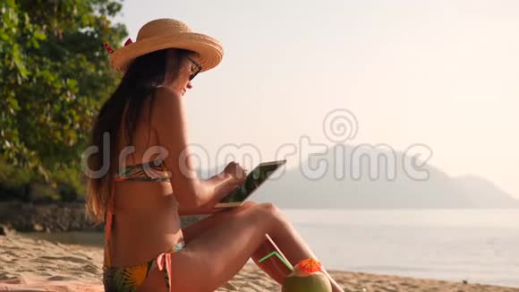 年轻的混合种族旅游女孩使用移动平板小猫和日光浴在热带海滩4K慢动作普吉岛视频的预览图