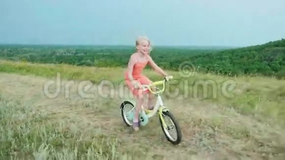 一个穿着粉红色连衣裙的酷女孩在乡下骑自行车村里无忧无虑的童年慢动作4k视频视频的预览图