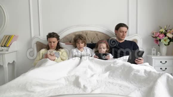 家长和孩子一起使用移动设备在卧室在周末在家有孩子的年轻夫妇视频的预览图