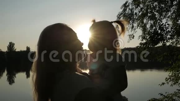 日落时分一个女人抱着一个小女孩在湖边亲吻她视频的预览图