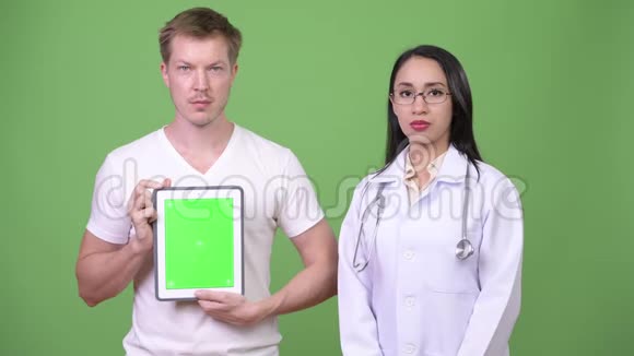 年轻的亚洲女性医生年轻的男性病人显示数字平板电脑视频的预览图