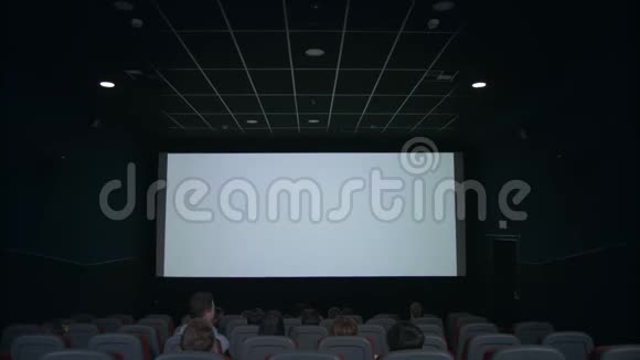 观众在电影院大厅观看白色屏幕期待电影放映视频的预览图