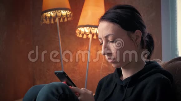 在家里的椅子上用智能手机的漂亮女孩视频的预览图