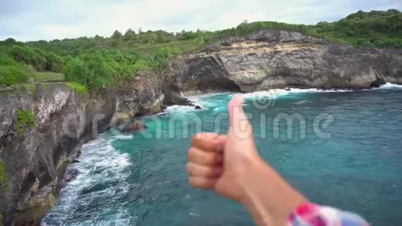 在美丽的风景背景下高高的悬崖海浪上展示拇指的人视频的预览图